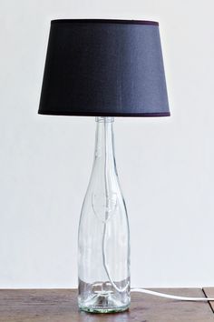 a glass bottle with a black shade on it sitting on a wooden table next to a lamp