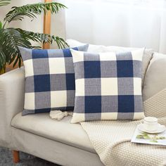 two blue and white checkered pillows on a couch next to a potted plant