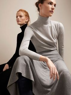 two women sitting next to each other wearing long dresses and turtleneck sweaters,