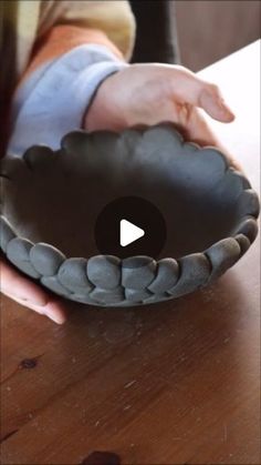 a person holding a black bowl on top of a wooden table next to a hand