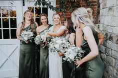 a group of women standing next to each other in front of a brick wall holding bouquets