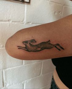 a woman's arm with a tattoo of a running rabbit on the left side