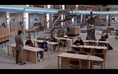 children are sitting at desks in the library with bookshelves and sculptures behind them