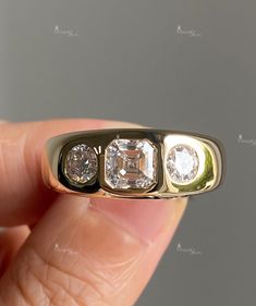 a hand holding a three stone ring in it's left hand, with the center diamond surrounded by four smaller stones