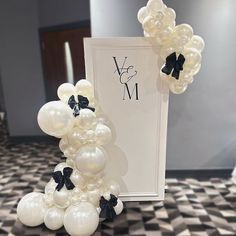 an arrangement of white balloons and black bows on a table with a card in the background