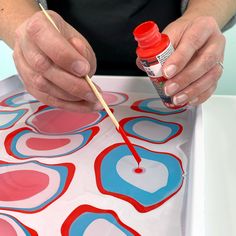 a person painting with red, white and blue circles on a sheet of paper while holding a brush