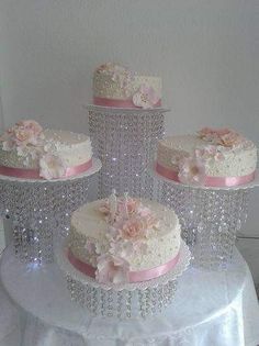 three tiered wedding cake with pink flowers and pearls on the top, sitting on a white tablecloth