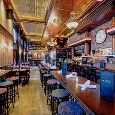 an empty restaurant with wooden tables and stools in front of the bar, along with clock on the wall