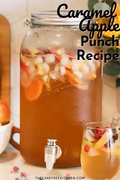 a glass jar filled with liquid next to a bowl of apples and oranges on a counter