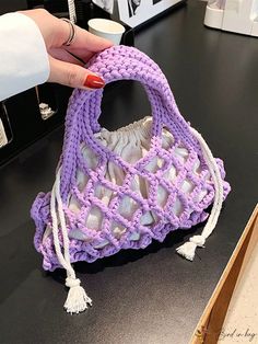 a hand holding a crocheted purse on top of a table next to a cup