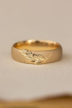 a gold wedding band with leaves on the side and a plain surface in the background