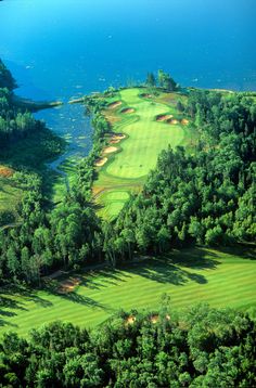 an aerial view of a golf course with water in the background and trees surrounding it