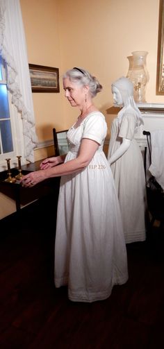 "This lovely underdress is made from two different fabrics which were sewn together to create what we know as a bodiced petticoat. The plain fabric bodice is constructed like a bib-front gown with a wide waistband. The sleeves are particularly snug and short, so they would not interfere with the sleeves of the dress or spencer worn over them. The skirt is made from a heavy dimity with 4 hem tucks and is easily worn as an outer garment. Its linen waist band was sewn to the interior of the cotton Regency Style Dress With Empire Waist And Historical Design, Regency Style Empire Waist Dress With Historical Design, Regency Prairie Dress With Empire Waist For Wedding, Daywear Dresses With Historical Design And Fitted Bodice, Regency Style Prairie Dress With Empire Waist For Weddings, Regency Style Empire Waist Prairie Wedding Dress, Historical Cotton Costume Dress, Fitted Regency Style Prairie Dress With Empire Waist, Historical Empire Waist Fitted Dress