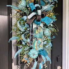 a blue and black wreath on the front door is decorated with feathers, leaves, flowers, and ribbons