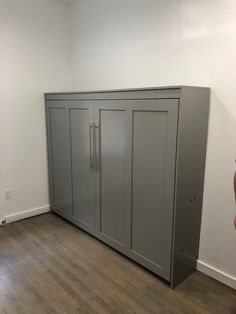 an empty room with two tall gray cupboards and a hard wood floor in front of it