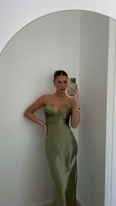 a woman in a green dress taking a selfie with her cell phone while leaning against a wall