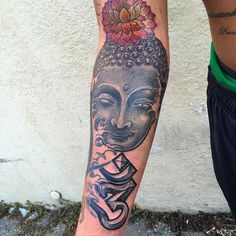 a man with a tattoo on his arm and leg has a buddha head in front of him