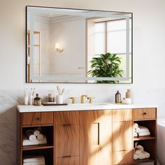 a bathroom with a large mirror above the sink and wooden cabinet below it, along with white towels