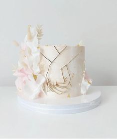 a white cake decorated with flowers and gold leaf accents on a plate against a plain background