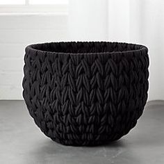 a large black basket sitting on top of a cement floor next to a white wall