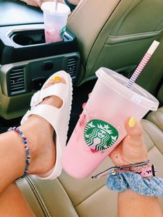 a person sitting in the back seat of a car holding up a pink starbucks drink