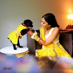 a woman in yellow dress petting a small black dog on top of a table