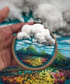 a hand holding a small embroidered keychain with an image of a volcano in the background