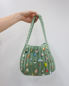 a hand holding a green crocheted purse with buttons on the front and sides