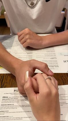 two people sitting at a table with papers and pens in front of them, one holding the other's hand