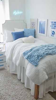 a white bed with blue and white decor in a small room, along with two framed pictures on the wall