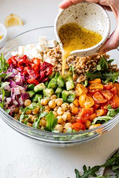 someone pouring dressing into a salad in a bowl with vegetables and chickpeas on the side