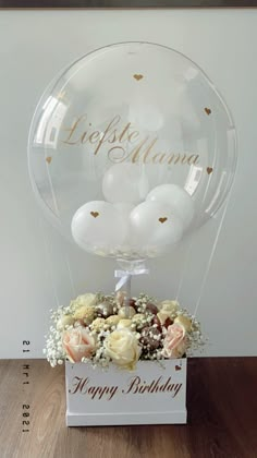 a clear balloon filled with white balloons and flowers on top of a wooden table next to a sign that says happy birthday