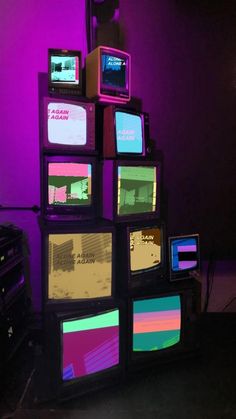 several televisions are stacked on top of each other in front of a purple wall