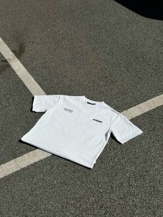 a white t - shirt laying on the ground in an empty parking lot next to a car