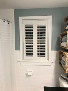 a white toilet sitting next to a bath tub under a window with shutters on it