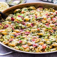 a pan filled with pasta and vegetables on top of a table next to utensils