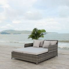 a couch sitting on top of a stone floor next to the ocean with a palm tree