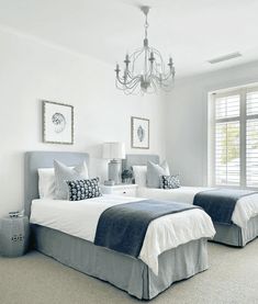 two beds in a bedroom with blue and white bedding, chandelier and windows