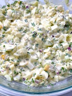 a glass bowl filled with potato salad on top of a wooden table next to utensils