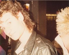 a young man wearing a leather jacket standing in front of a woman with blonde hair