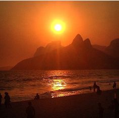 the sun is setting at the beach with people playing in the water and on the sand