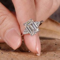 a woman's hand with a diamond ring on top of her finger and an engagement ring in the middle