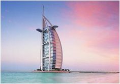 a very tall building in the middle of the ocean with a pink sky behind it