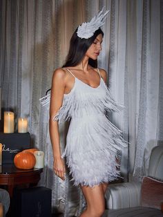 a woman in a white feathered dress standing next to a table with candles on it