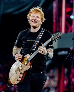 a man with red hair holding a guitar and smiling at the camera while standing in front of an audience