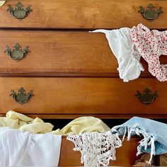 an old dresser with clothes hanging from it's handles and lace on the drawer