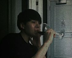 a man drinking from a wine glass in front of a door with the light on