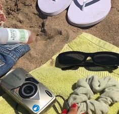 someone is sitting on the beach with their flip flops and camera next to them