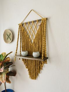 a wall hanging on the side of a white wall next to a potted plant