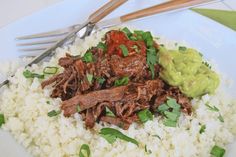 a white plate topped with rice and meat next to a fork on top of a table